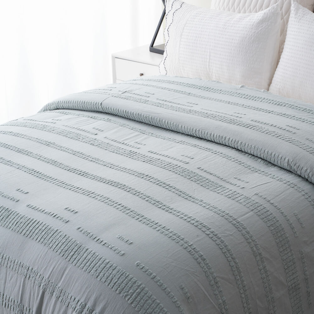 Close-up of sage green recycled tufted cotton linen duvet set on a bed with white pillows.