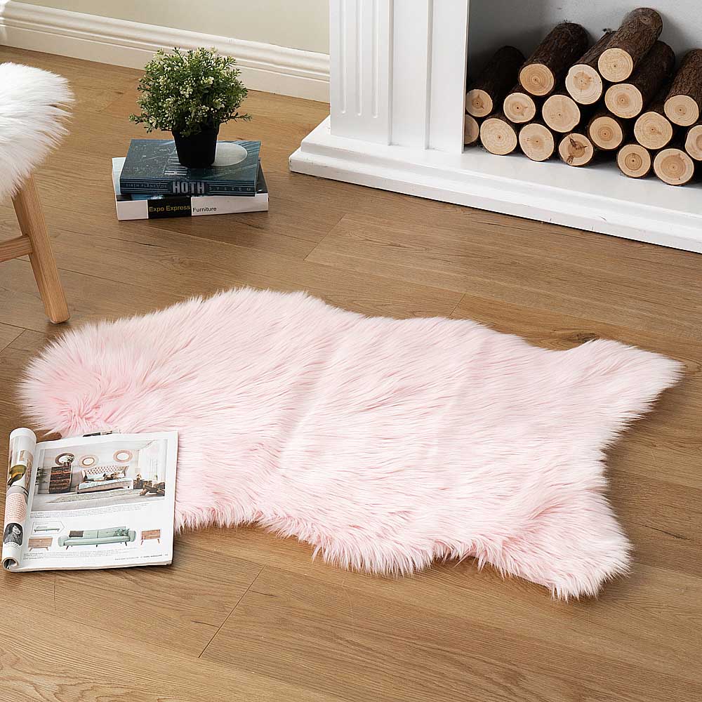 Soft pink faux sheepskin area rug shaped irregularly near a fireplace decor, ideal for home decor bulk import.
