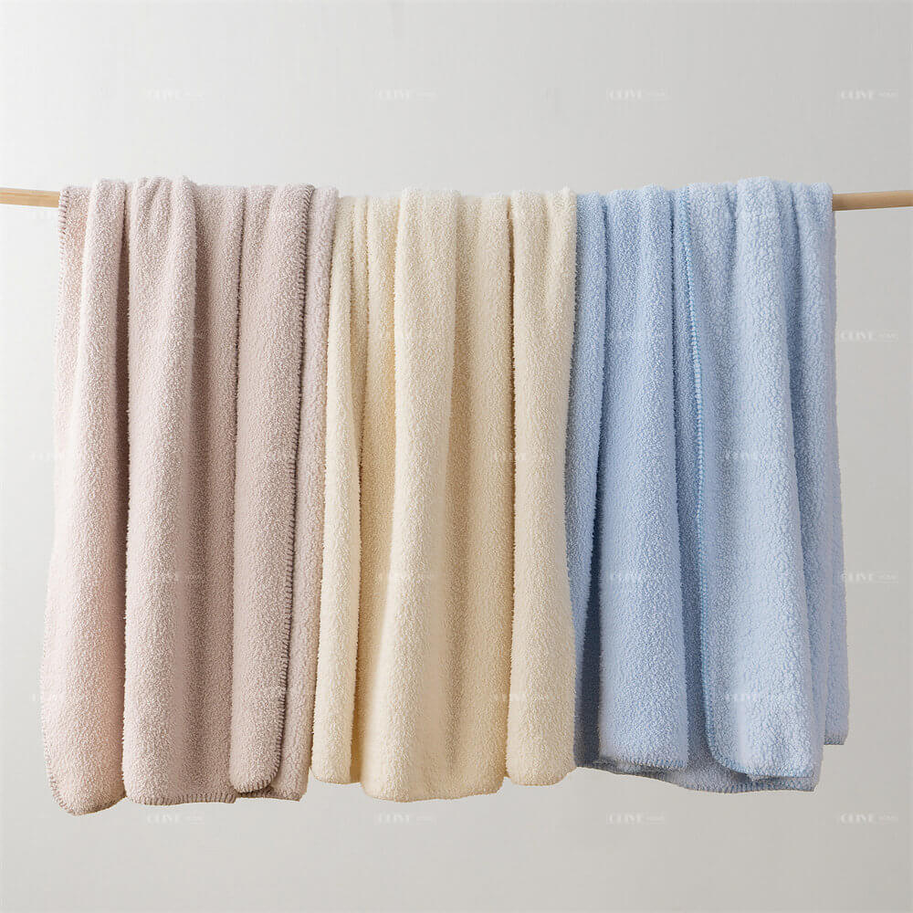 Pastel pink, cream, and soft blue microfiber chenille reversible throw blankets hanging on a rack for custom manufacturing.