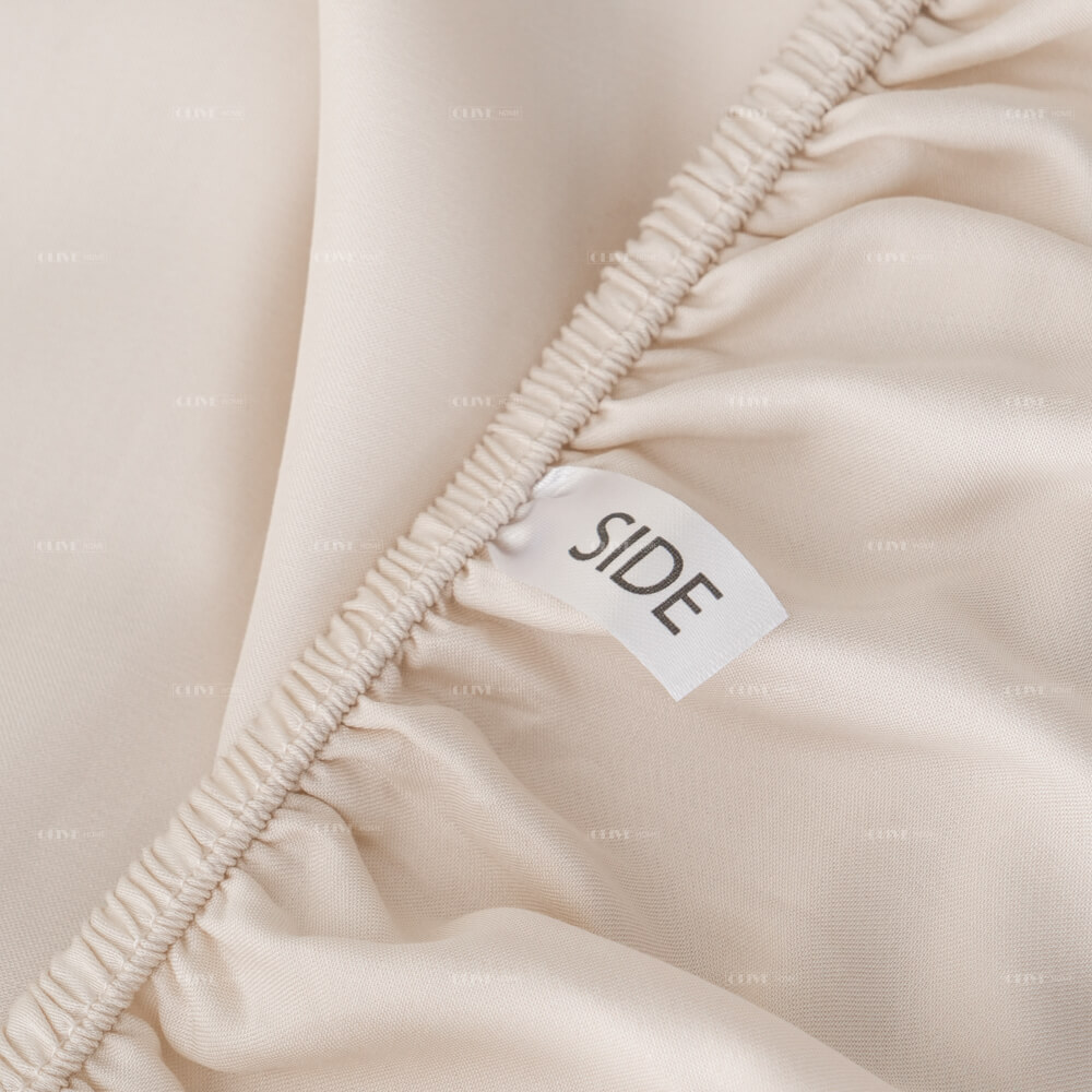 Close-up of the deep pocket fitted sheet corner made of bamboo fabric, featuring a durable elastic band and a smart 'SIDE' indicator label for easy bedmaking.