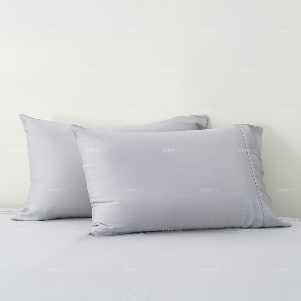 Two light grey organic bamboo pillowcases stacked neatly on a matching bamboo bed sheet.