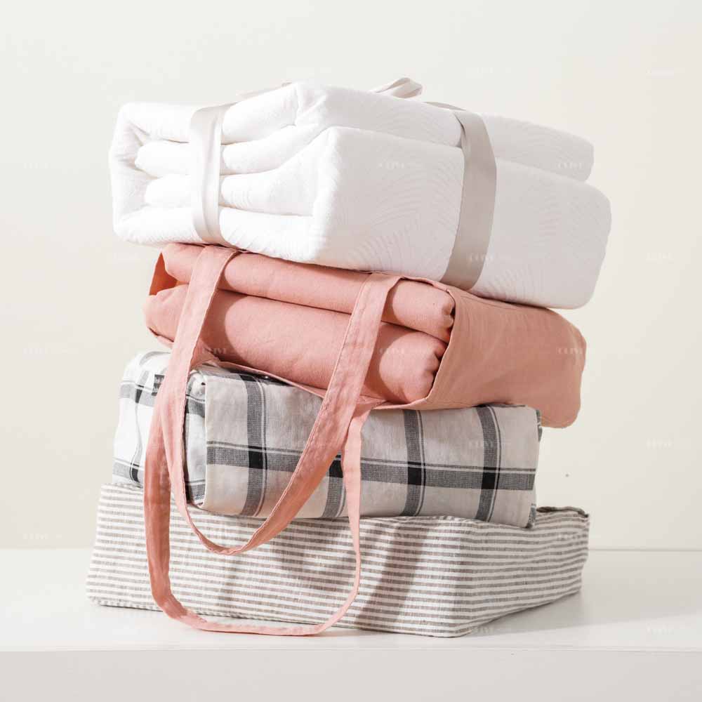 A stack of multi-colored premium French flax linen bedding sets in reusable bags, bulk custom production from home textile manufacturer.