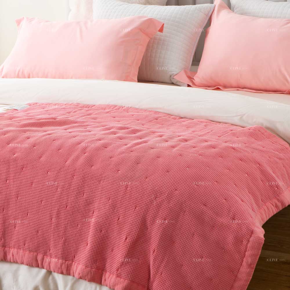 Close-up of Peachy Pink Mills waffle cotton quilt with dot quilting and matching pillowcases displayed on a white bed