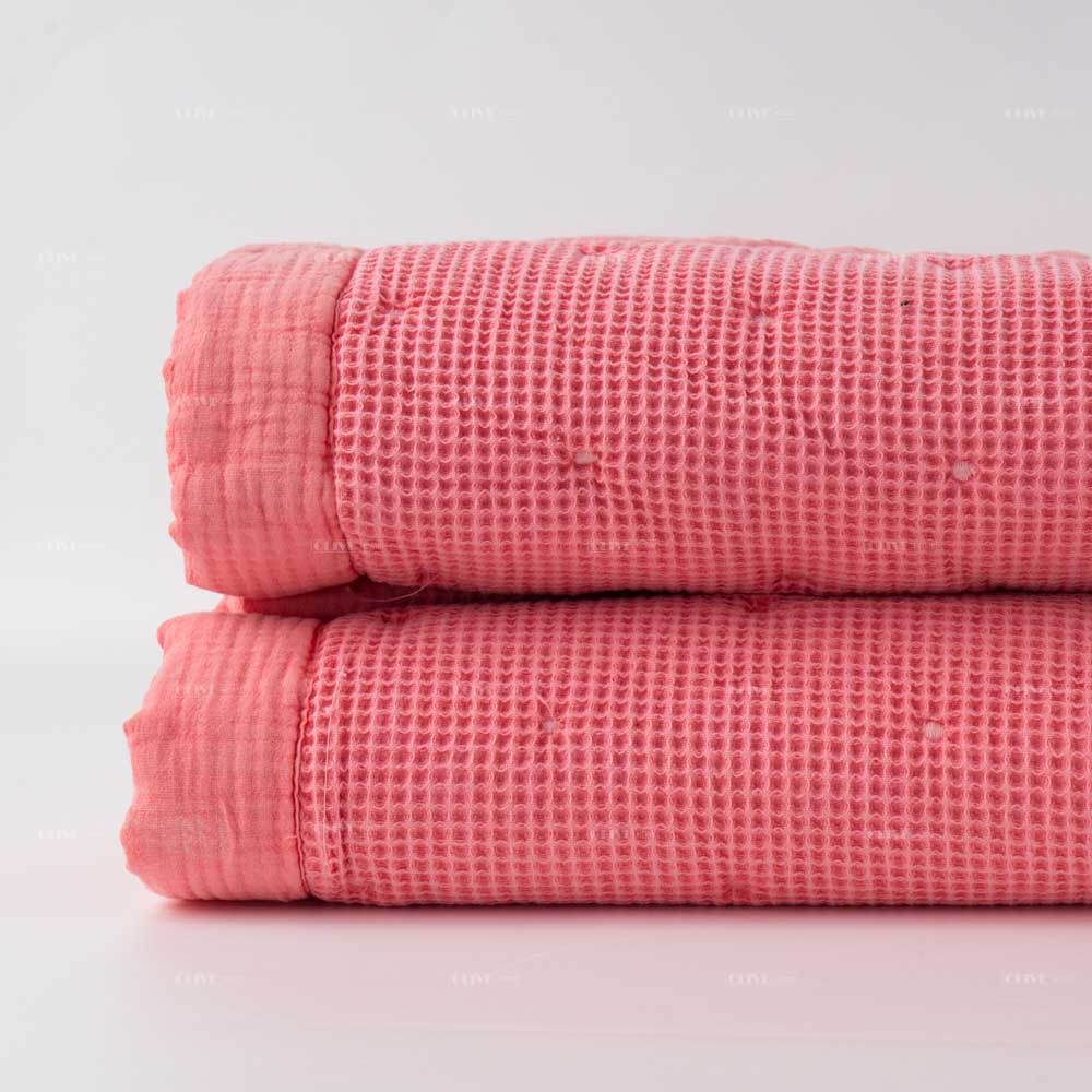 Folded peachy pink waffle cotton quilt showing honeycomb texture and durable fabric binding