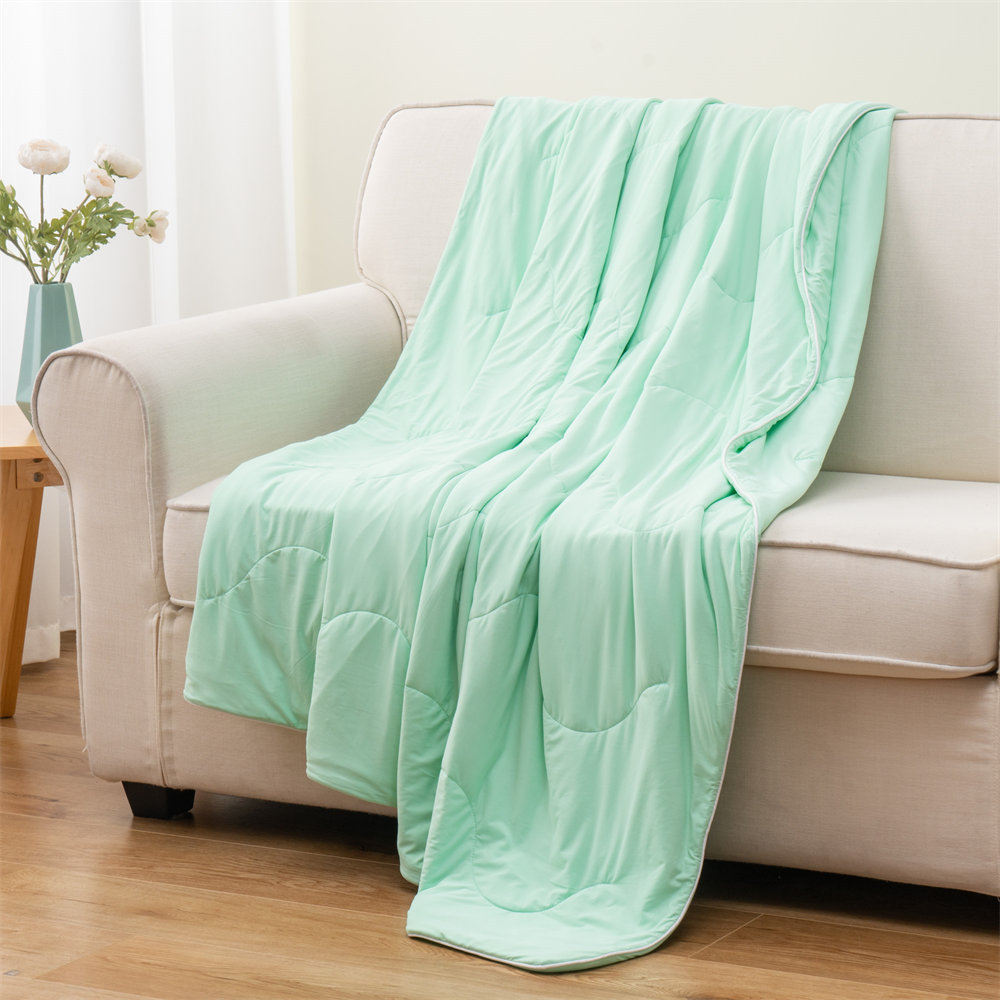 Bulk wholesale lightweight cooling comforter in mint green draped on a modern sofa, high-quality summer bedding supplier