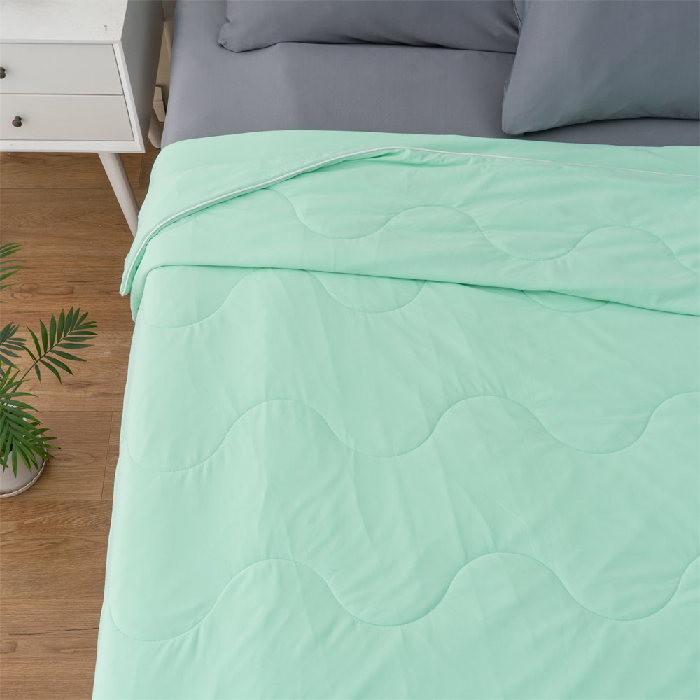 Top view of mint green lightweight cooling comforter on bed, elegant wave-stitched summer blanket from direct bedding manufacturer